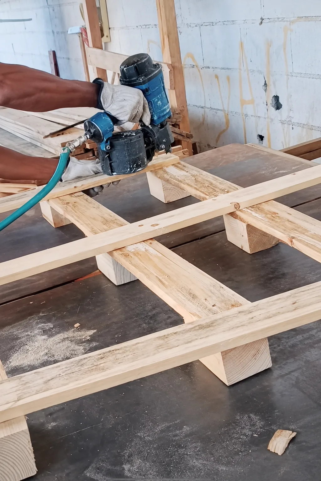 Close view of a pneumatic coil nailer and gloved hands at a wooden pallet joint